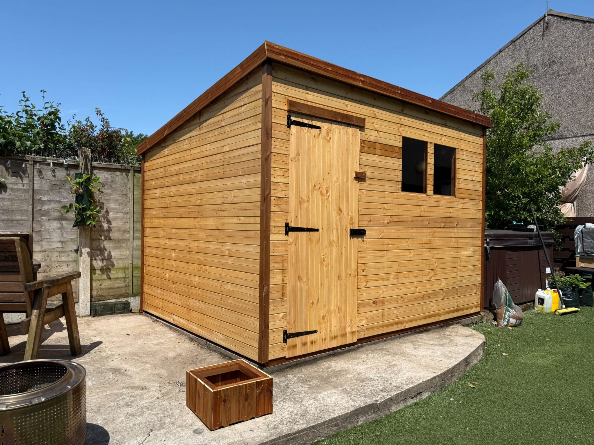 Timber garden shed shown from side angle, featuring shiplap cladding, felt roof, and secure door hinges.