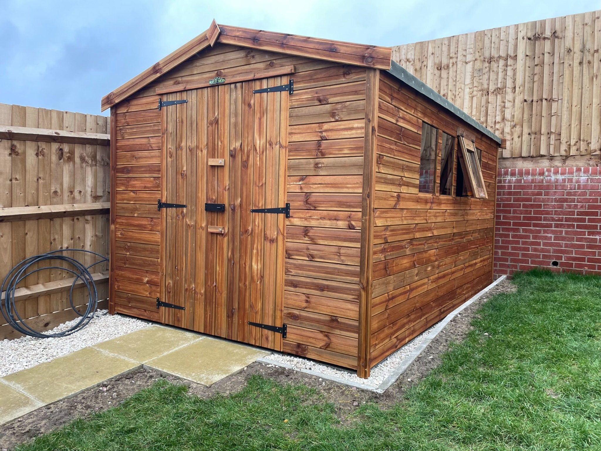 Wooden garden shed with double doors and apex roof, installed on a concrete base in a residential garden.