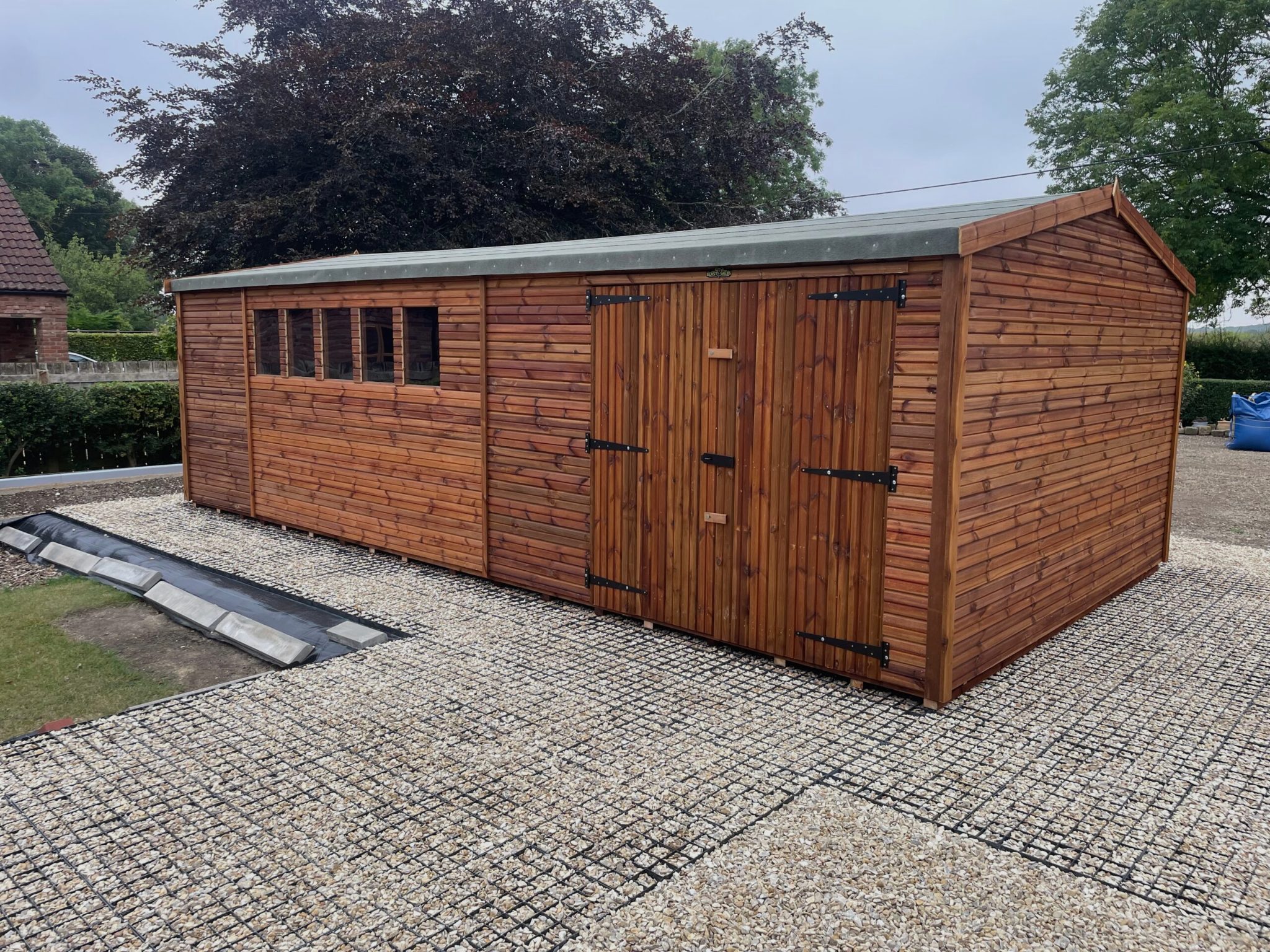 Wooden garden shed with double doors and apex roof, installed on a concrete base in a residential garden.
