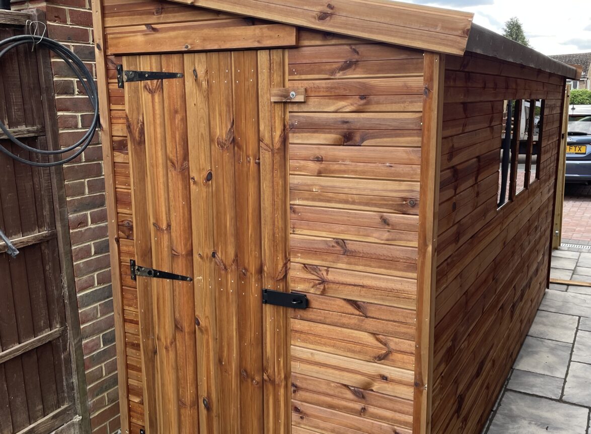 A small pent garden shed with 3 windows and a single door