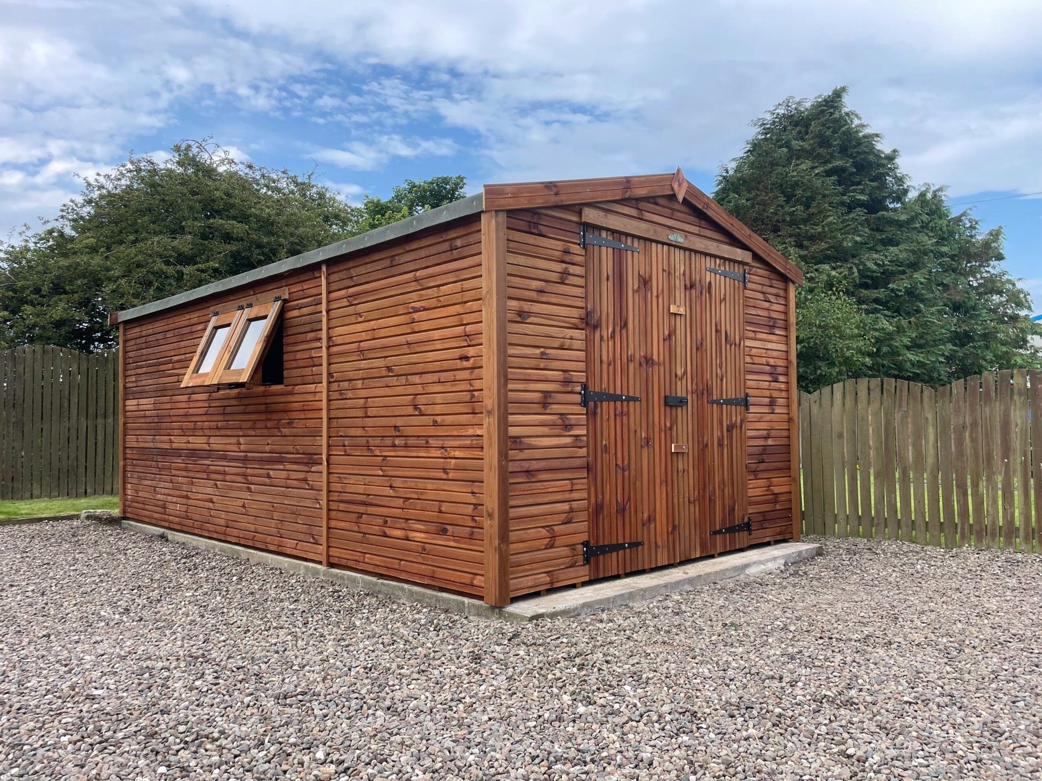 Wooden garden shed with double doors and apex roof, installed on a concrete base in a residential garden.