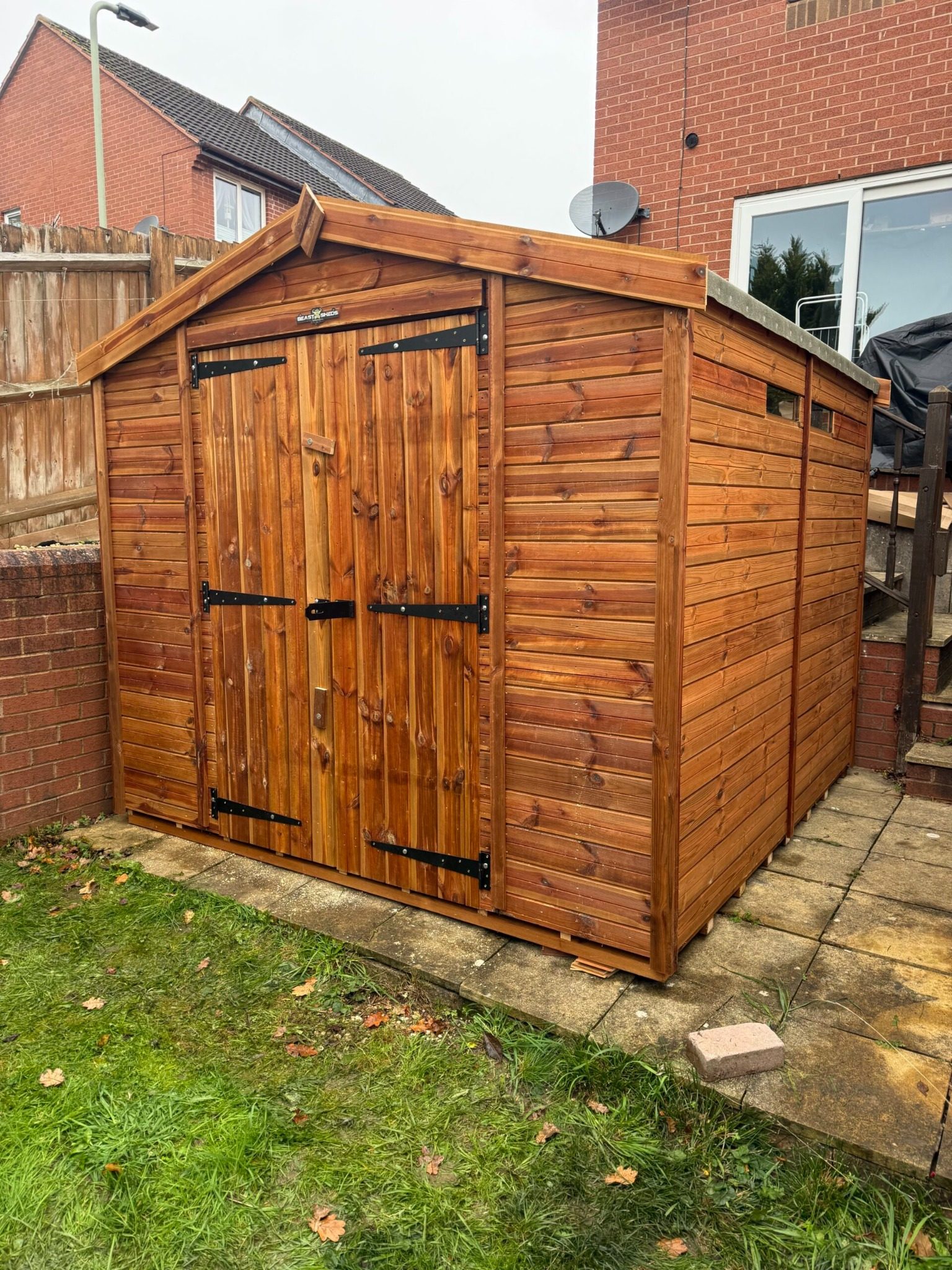 Wooden garden shed with double doors and apex roof, installed on a concrete base in a residential garden.